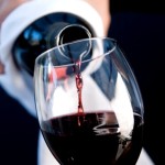 Close up of a waiter hands holding a bottle and pouring red wine in a glass